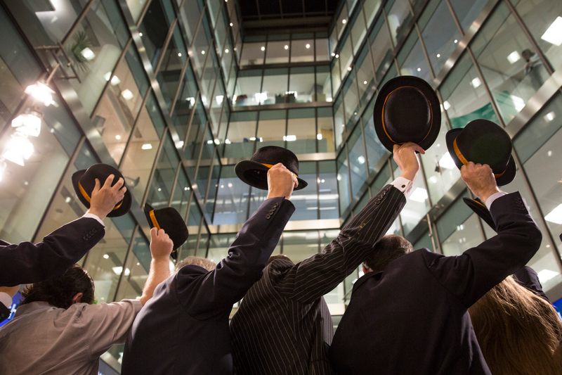 Men are raising bowler hats in front of the London Stock Exchange