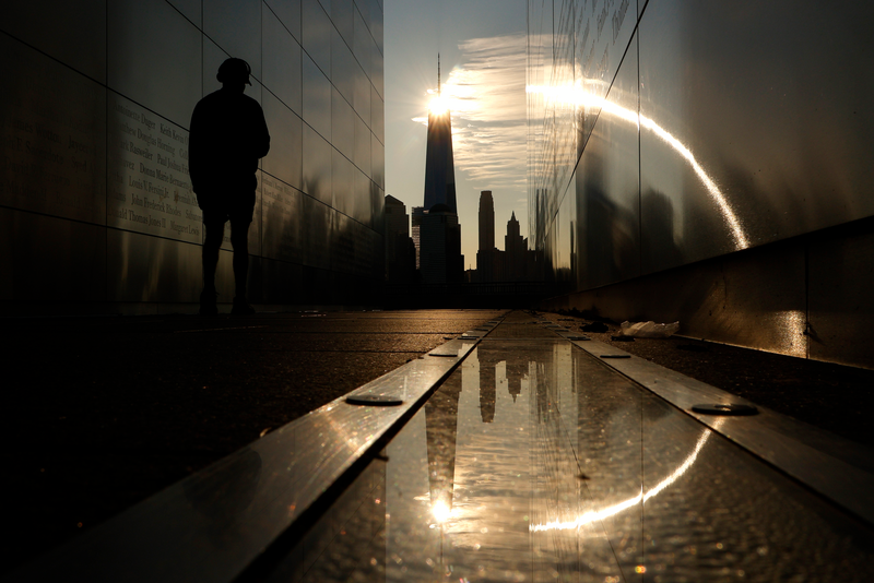 The sun rises behind the skyline of lower Manhattan and One World Trade Center in New York City as a person walks through the Empty Sky 9/11 Memorial on July 22, 2023, in Jersey City, New Jersey. (