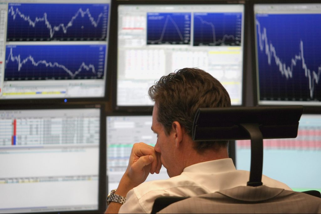 Image of man in front of several computer screens, watching stock price movement.
