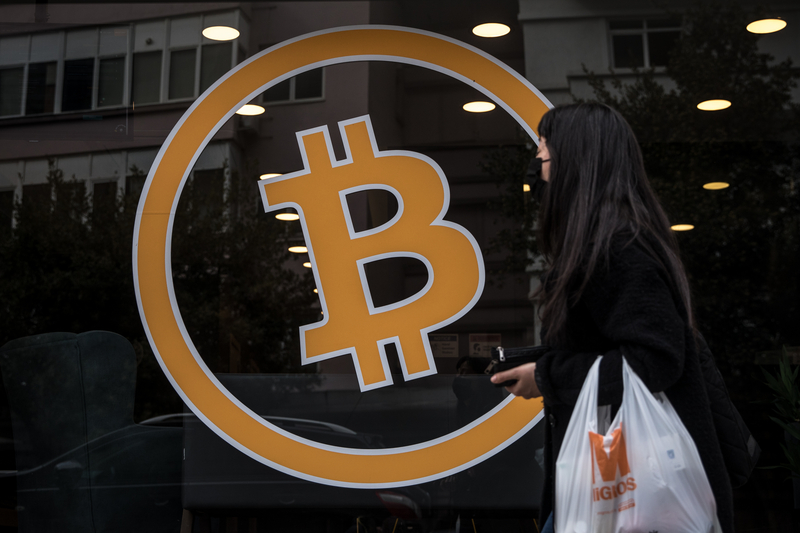 Woman walking by a big Bitcoin sign displayed on a window.