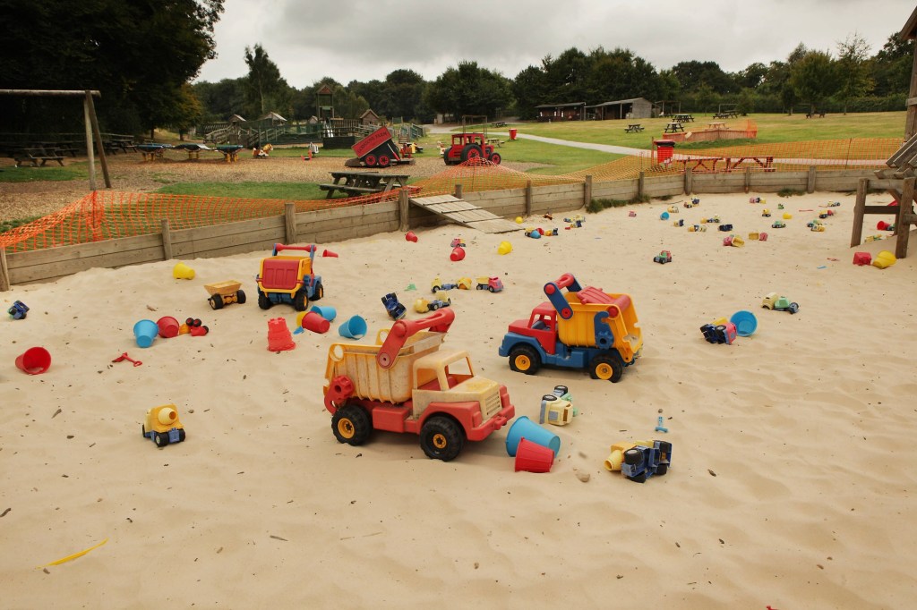 Image of a kid's sandbox with some toy cars and trucks in it