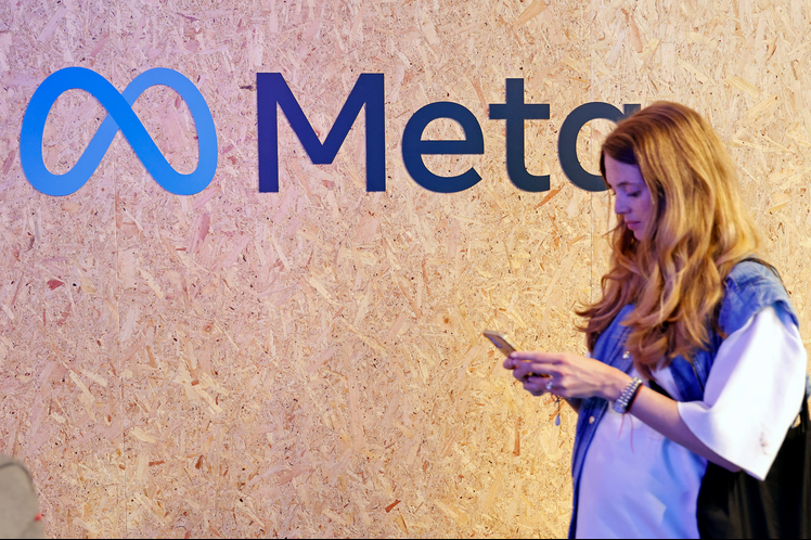 A girl stands in front of the Meta logo.