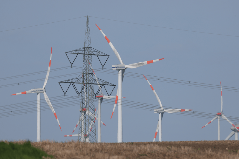 An electricity pylon stands near wind turbines spinning at a wind farm on May 02, 2024 near Altentreptow, Germany.