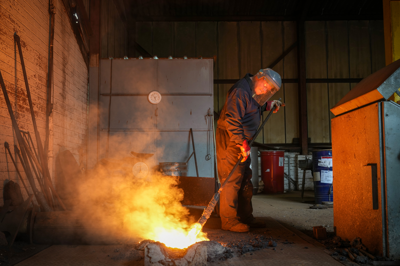 A furnaceman removes slag from molten iron.