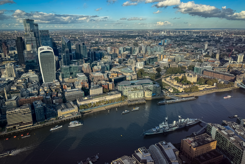 High rise buildings in historic City of London financial district including the Walkie-Talkie dominate the skyline beside the River Thames.