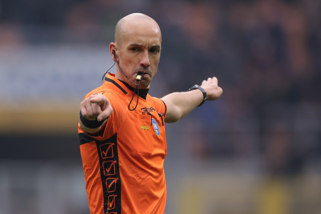 Image of a soccer referee in an orange shirt with a whistle.