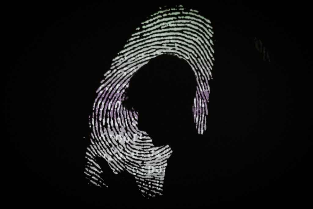 Image of a fingerprint looming as an image on a black screen with a silhouette of a person in front of it.