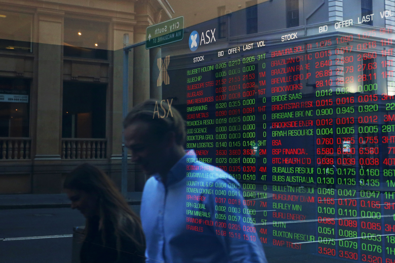 Pedestrians are reflected in a window as electronic boards display stock information at the Australian Securities Exchange, operated by ASX Ltd.