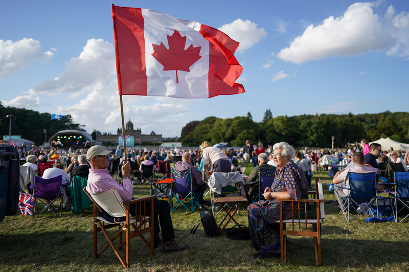 A couple sit with the Canadian national flag at an outdoor concert.