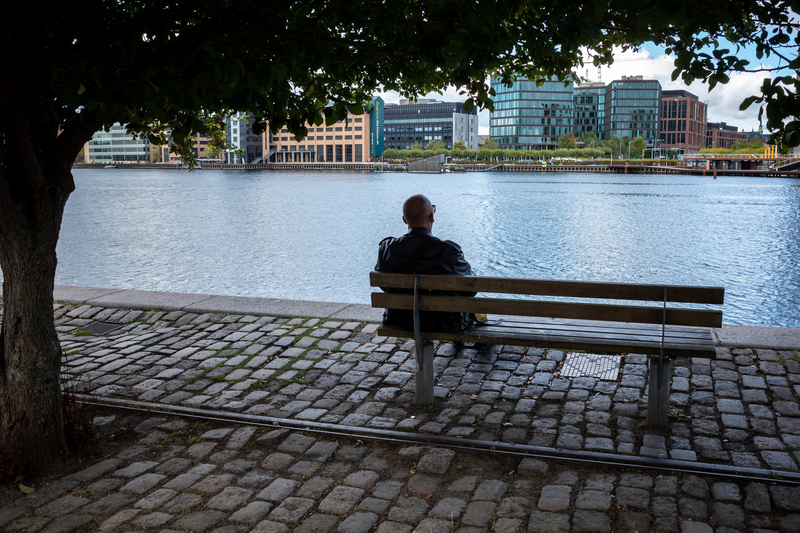 A man sits alone on a bench in the Copenhagen harbor in Denmark.