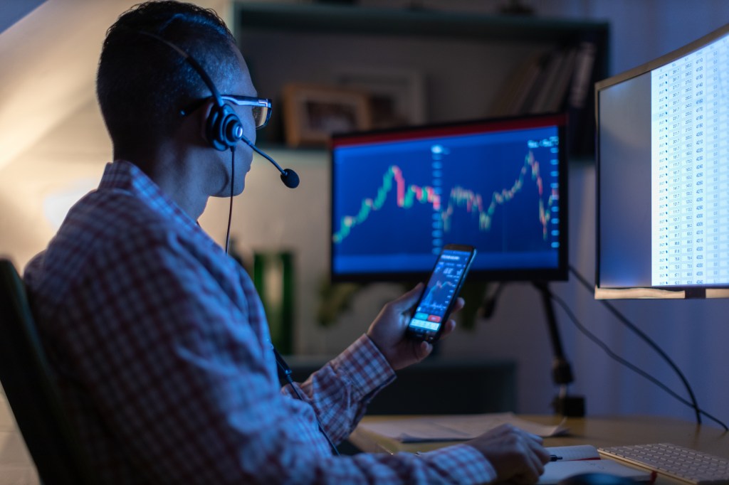 Man looking at currency trading app on his smart phone from his home office