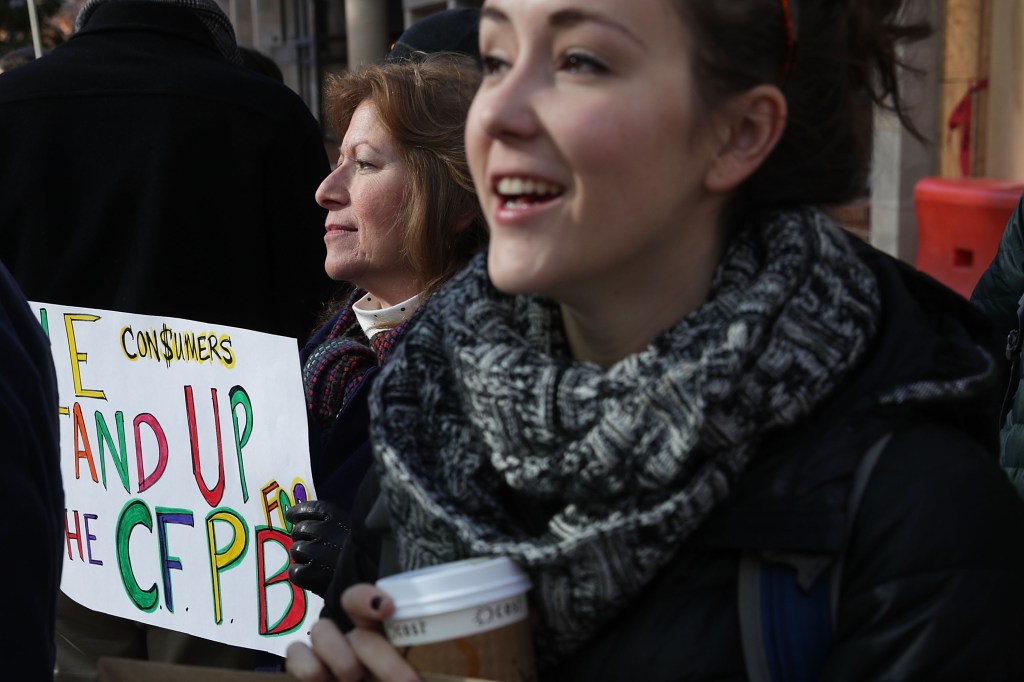 Image of a woman holding a sign saying "Consumers Stand Up for the CFPB."