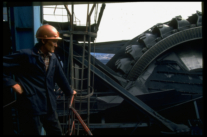 Open pit coal mine worker framed by Russian-made bucket wheel excavator operating at 1 of world's largest coal mine ops, in Central Steppes region.