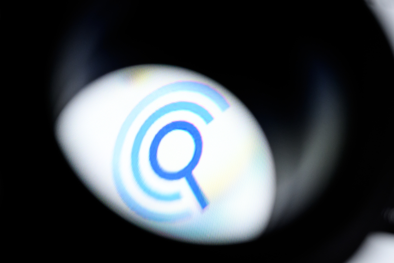 The logo of the data broker company Clearview.AI is seen through a magnifying loupe as it is displayed on a screen.